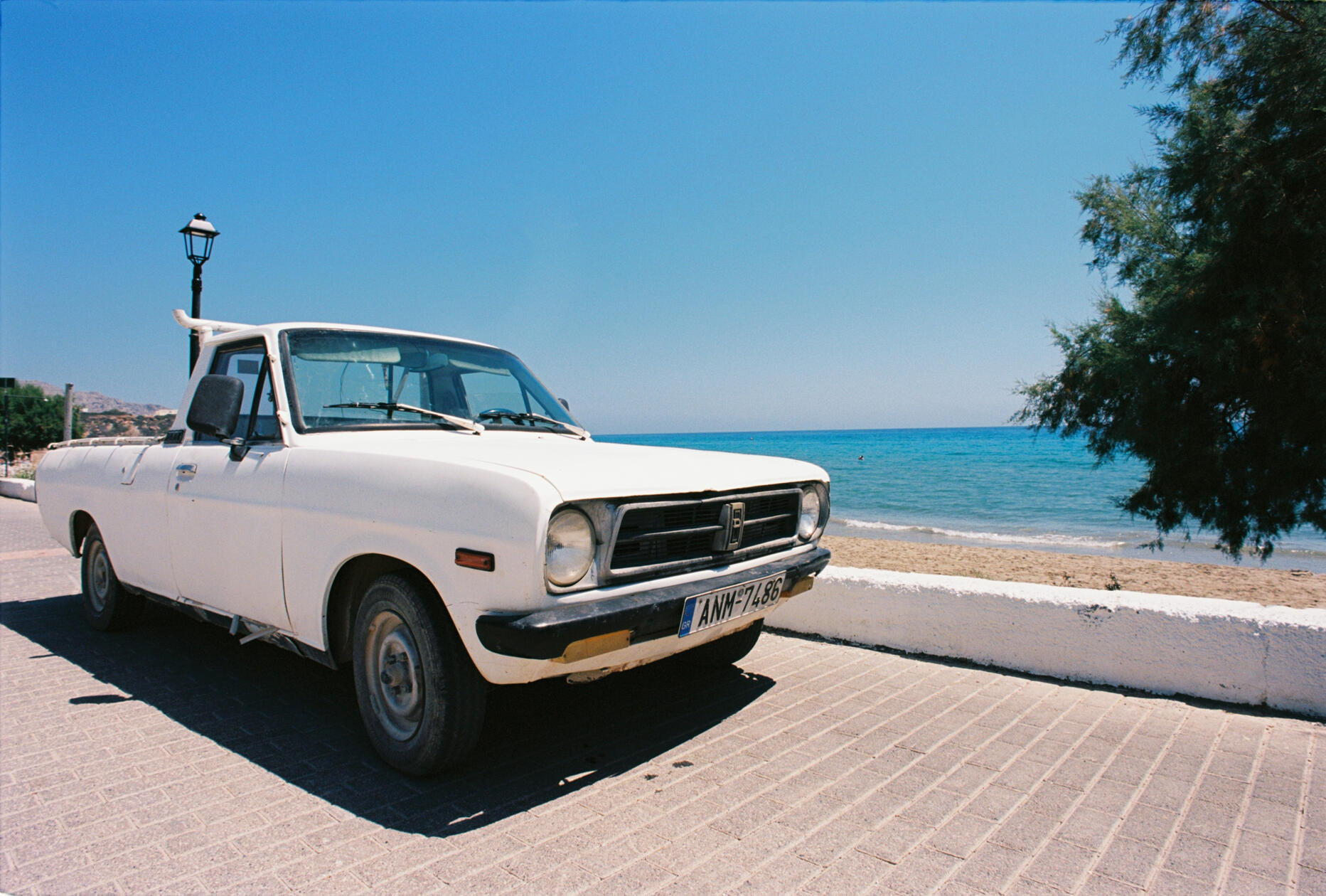 Vintage Datsun truck parked by sun-drenched beach in southern Crete, captured on analog film with Nikon F5